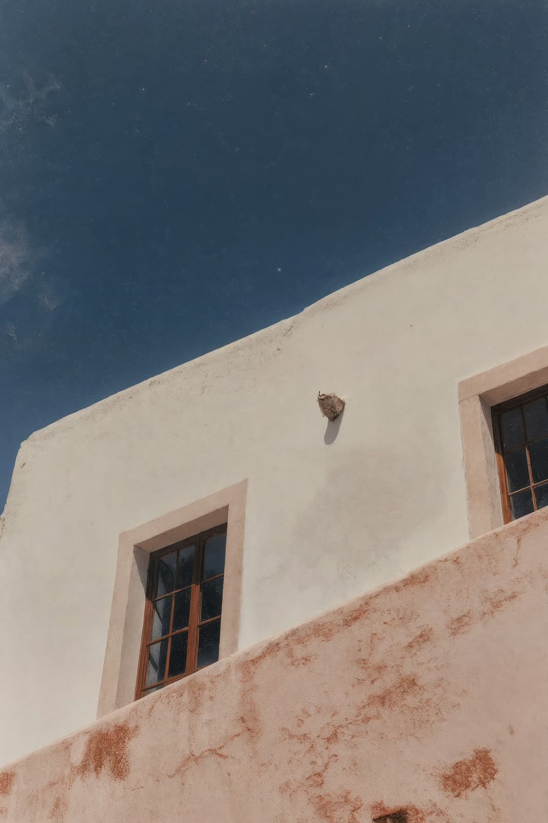 White and pink stucco walls with wooden windows under a deep blue sky