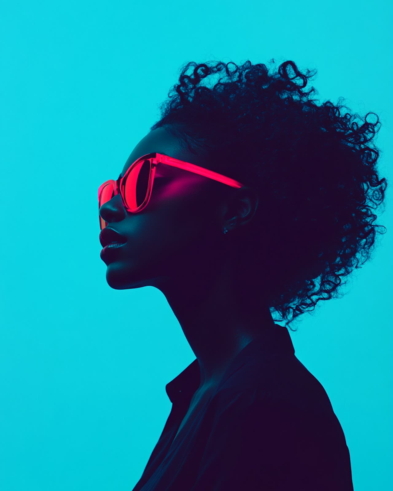 A woman in neon pink sunglasses in profile against a vibrant blue background